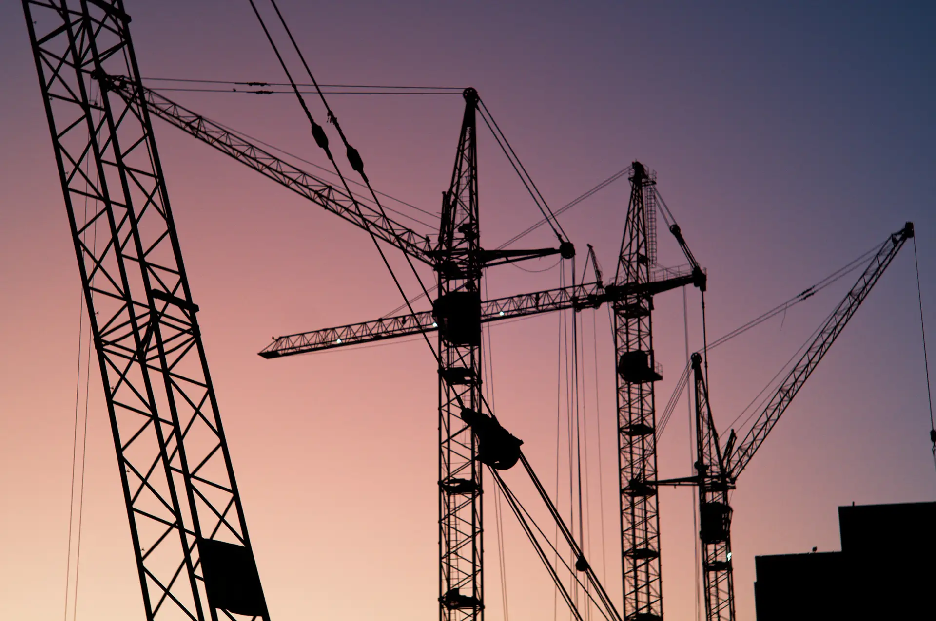 Construction cranes silhouetted against a dusk sky
